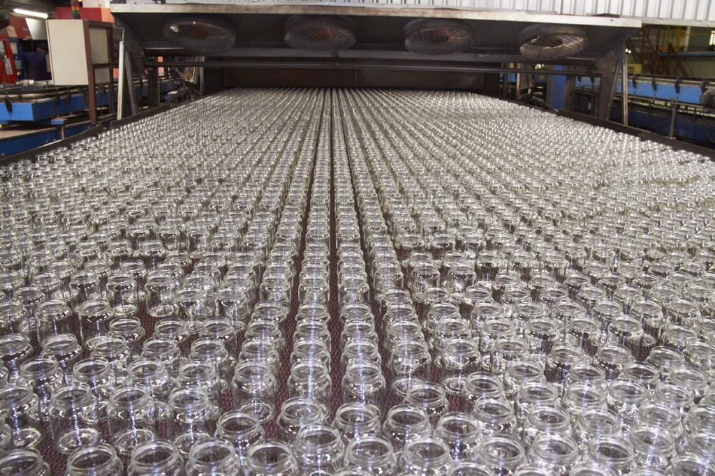Rows of empty clear glass bottles moving along the cold-end conveyor after the annealing lehr