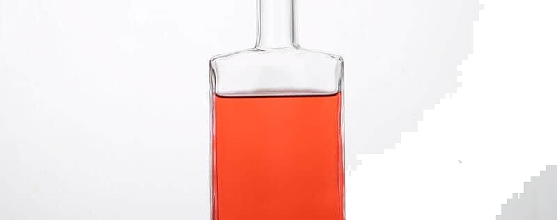 Square heavy-based liquor bottle in clear glass, filled with a rose-coloured spirit